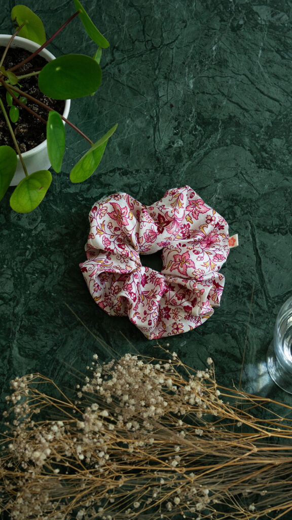 Scrunchie har et pink og orange blomstret print på en lys baggrund. Den har en god stretch.